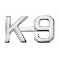 Metallic rank insignia featuring a K-9 design, constructed from metal with a silver finish. Measures 1/2 in and attaches to fabric via a clutch pin. Suitable for use on uniforms to denote K-9 unit roles