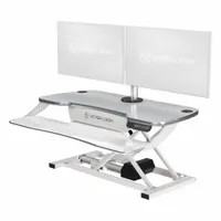This electronic standing desk converter from VERSADESK features a white wood desktop measuring 36 inches wide by 24 inches deep. It allows users to alternate between sitting and standing positions at a fixed desk, promoting ergonomic comfort in office, home, or industrial settings