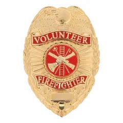 This oval metal badge measures 2 1/4 inches by 3 1/8 inches and features a gold finish. It is constructed from metal and includes a pin with safety catch for attachment to uniforms. Commonly used as identification or recognition emblems for volunteer firefighters and similar personnel.