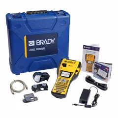 Handheld label printer with 1-inch print width and 300 dpi resolution. Includes battery, Brady Workstation software, magnet accessory, and indoor/outdoor vinyl label cartridge. Used for on-site identification of cables, panels, and equipment in industrial maintenance and facility management.